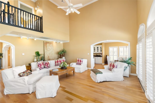 living room featuring crown molding, rail lighting, wood-type flooring, and a high ceiling