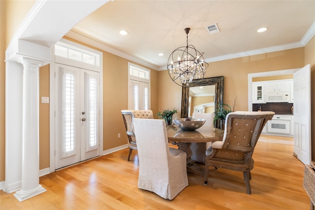 dining space featuring light hardwood / wood-style flooring, ornamental molding, a notable chandelier, and ornate columns