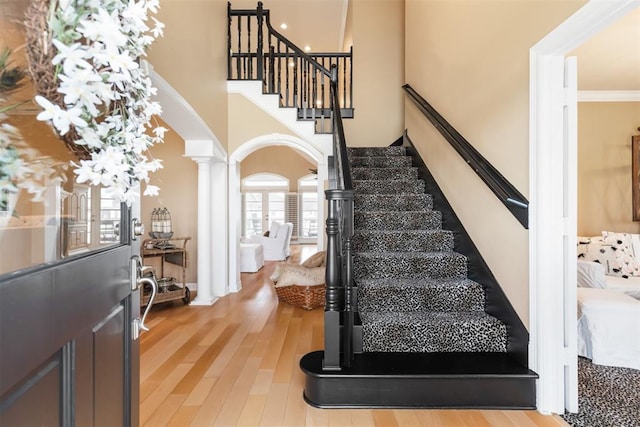 stairway featuring ornate columns, wood-type flooring, and ornamental molding