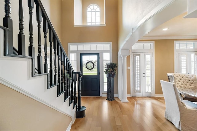 foyer with crown molding, ornate columns, light wood-type flooring, and a high ceiling