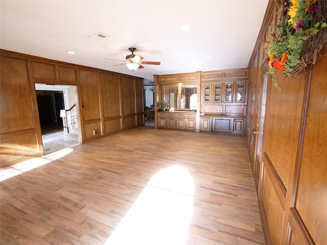 unfurnished living room with light wood-type flooring, ceiling fan, and wooden walls