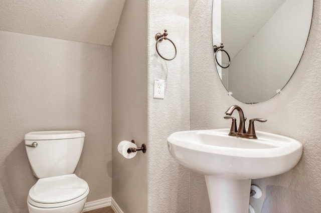 bathroom with toilet, a textured ceiling, sink, and vaulted ceiling