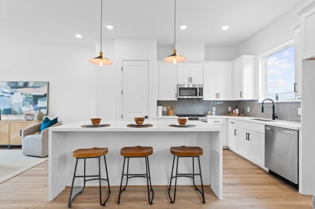 kitchen with white cabinetry, appliances with stainless steel finishes, pendant lighting, a kitchen island, and light wood-type flooring