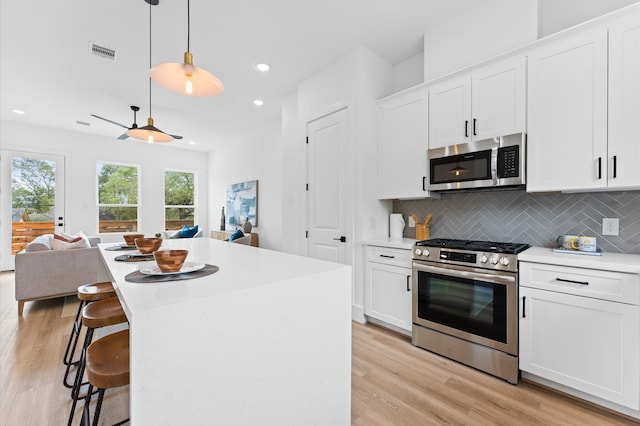 kitchen featuring white cabinets, stainless steel appliances, a kitchen island, and light hardwood / wood-style floors