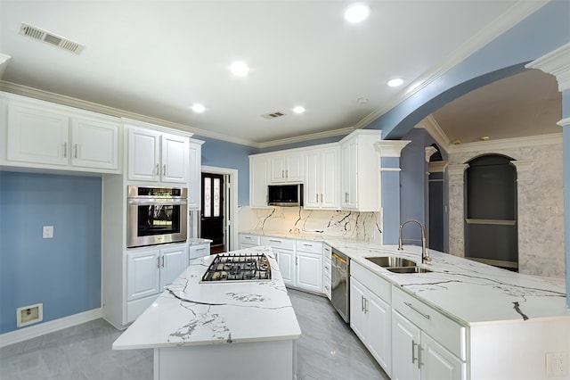 kitchen with kitchen peninsula, stainless steel appliances, sink, decorative columns, and white cabinets