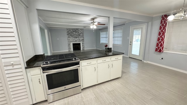 kitchen featuring a stone fireplace, decorative light fixtures, white cabinets, stainless steel range oven, and ceiling fan with notable chandelier