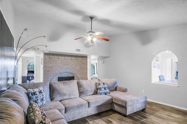 living room with ceiling fan, a textured ceiling, dark hardwood / wood-style flooring, and a brick fireplace