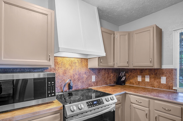 kitchen featuring a textured ceiling, premium range hood, stainless steel appliances, and backsplash