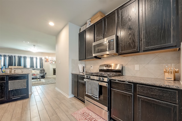 kitchen with backsplash, light stone countertops, dark brown cabinetry, and appliances with stainless steel finishes