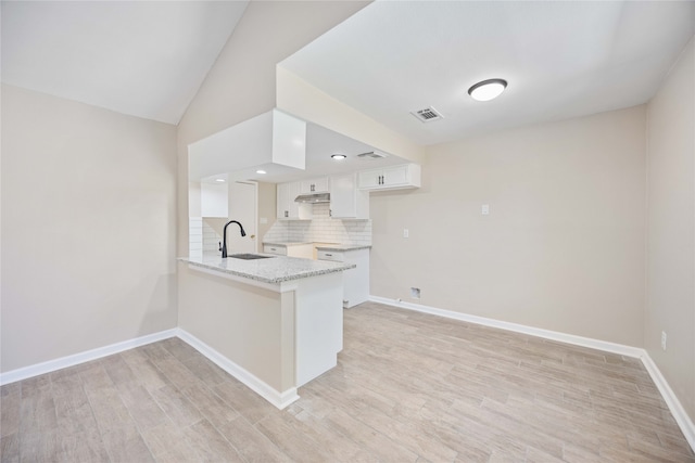 kitchen with kitchen peninsula, backsplash, sink, white cabinetry, and light hardwood / wood-style floors