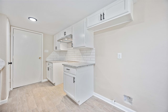 kitchen featuring light stone countertops, white cabinets, light hardwood / wood-style flooring, and backsplash