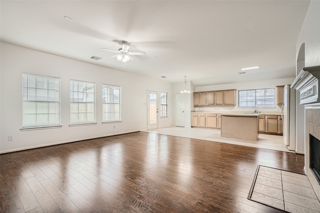 unfurnished living room featuring sink, ceiling fan with notable chandelier, a tiled fireplace, and light wood-type flooring