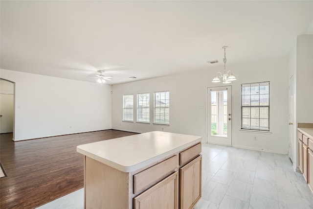 kitchen with light brown cabinetry, ceiling fan with notable chandelier, a center island, light hardwood / wood-style floors, and decorative light fixtures