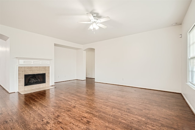 unfurnished living room featuring dark hardwood / wood-style floors, a tiled fireplace, and ceiling fan