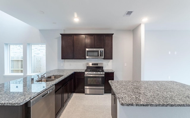 kitchen featuring kitchen peninsula, stainless steel appliances, backsplash, sink, and light stone counters