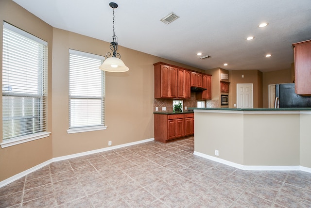 kitchen with a wealth of natural light, decorative backsplash, hanging light fixtures, and stainless steel refrigerator