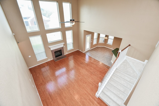 unfurnished living room featuring ceiling fan, a towering ceiling, a brick fireplace, and hardwood / wood-style floors