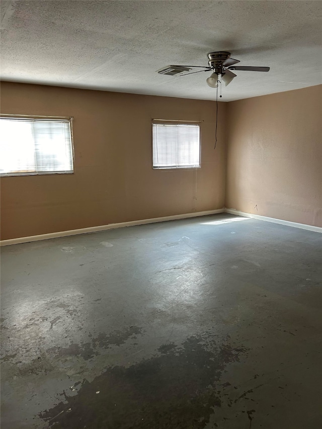 spare room with a textured ceiling, ceiling fan, concrete flooring, and a wealth of natural light