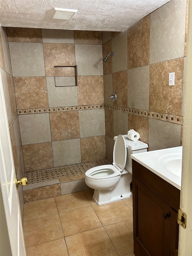 bathroom with a tile shower, a textured ceiling, toilet, tile walls, and vanity