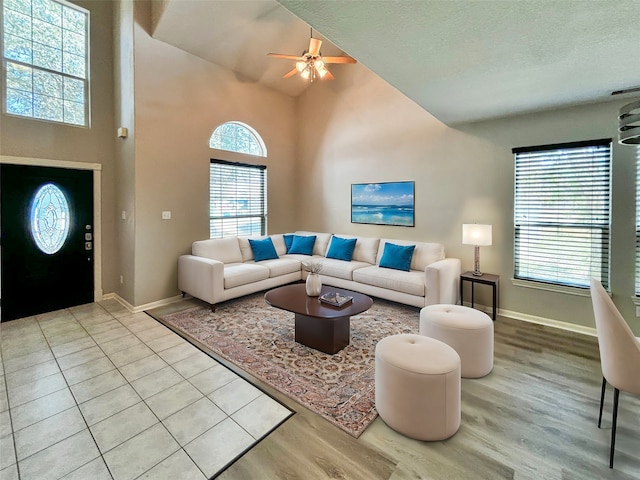 living room with light hardwood / wood-style floors, a textured ceiling, high vaulted ceiling, and ceiling fan