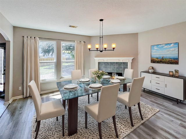 dining space featuring a tiled fireplace, wood-type flooring, a textured ceiling, and an inviting chandelier