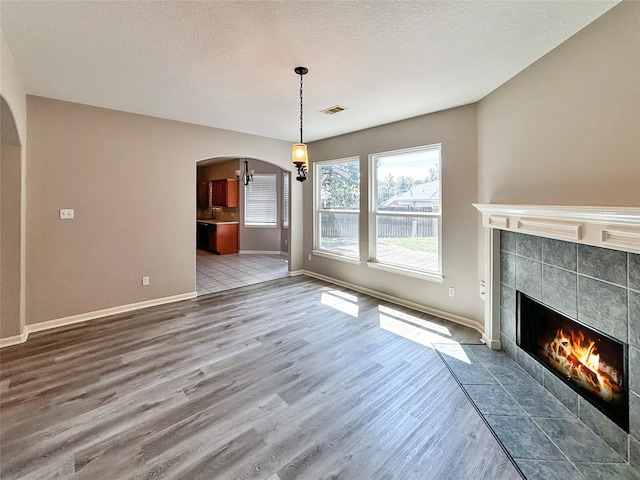 unfurnished living room with a tiled fireplace, a textured ceiling, and hardwood / wood-style floors