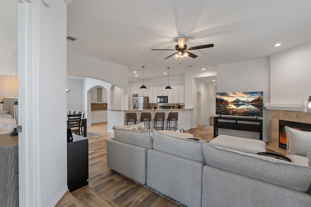 living room featuring ceiling fan, light wood-type flooring, and a fireplace