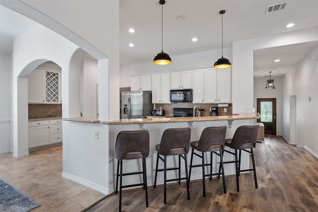 kitchen featuring decorative backsplash, hardwood / wood-style flooring, hanging light fixtures, black appliances, and white cabinets