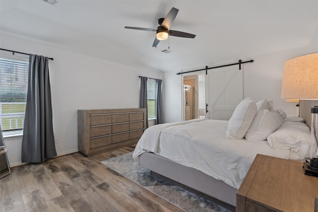 bedroom with a barn door, hardwood / wood-style flooring, and ceiling fan