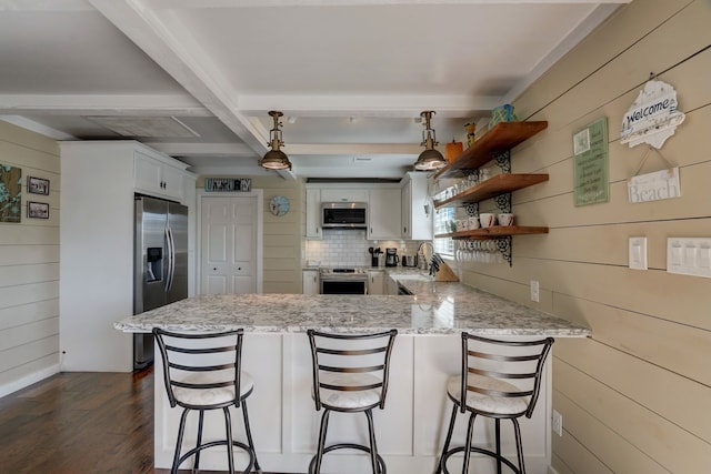 22819 Vida St, Galveston, TX 77554 - kitchen with stainless steel appliances, a peninsula, wood walls, dark wood-type flooring, and light stone counters
