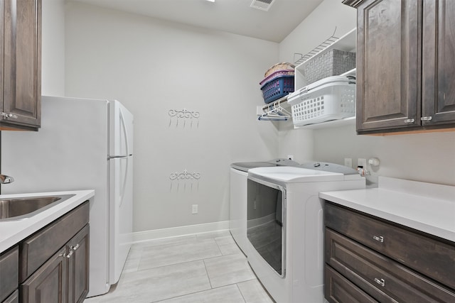 laundry area with independent washer and dryer, cabinets, sink, and light tile patterned floors