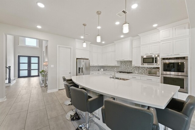 kitchen with french doors, an island with sink, a kitchen bar, decorative light fixtures, and appliances with stainless steel finishes