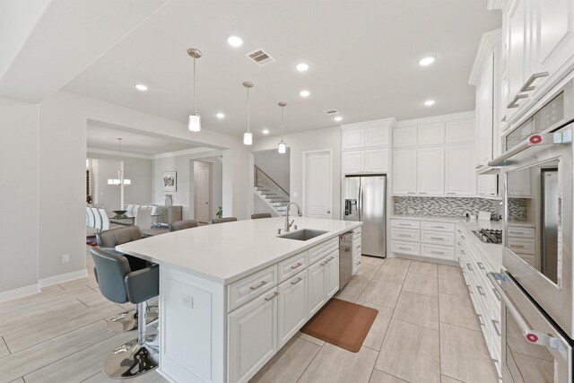 kitchen featuring appliances with stainless steel finishes, backsplash, a kitchen breakfast bar, white cabinets, and a center island with sink