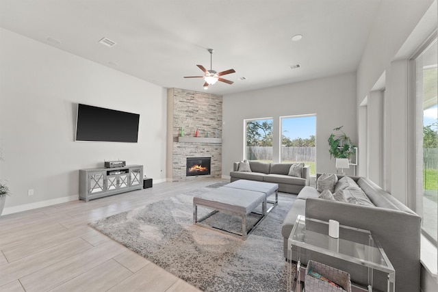 living room with light hardwood / wood-style flooring, a stone fireplace, and ceiling fan