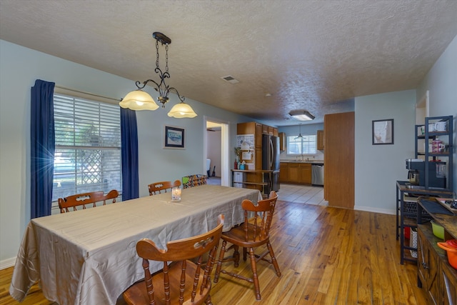 dining room featuring light hardwood / wood-style floors, an inviting chandelier, a textured ceiling, and sink