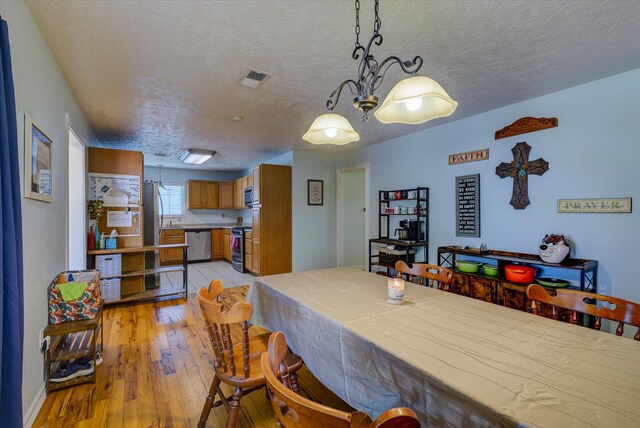 dining room with light hardwood / wood-style flooring, a notable chandelier, and a textured ceiling