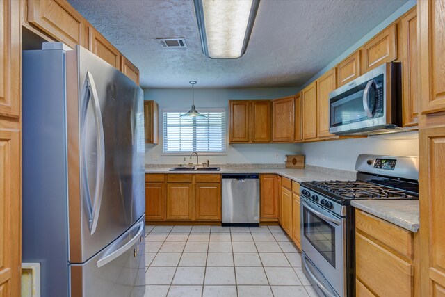 kitchen with appliances with stainless steel finishes, sink, a textured ceiling, pendant lighting, and light tile patterned floors