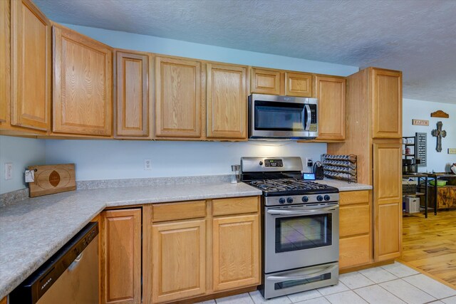 kitchen with a textured ceiling, appliances with stainless steel finishes, and light hardwood / wood-style flooring