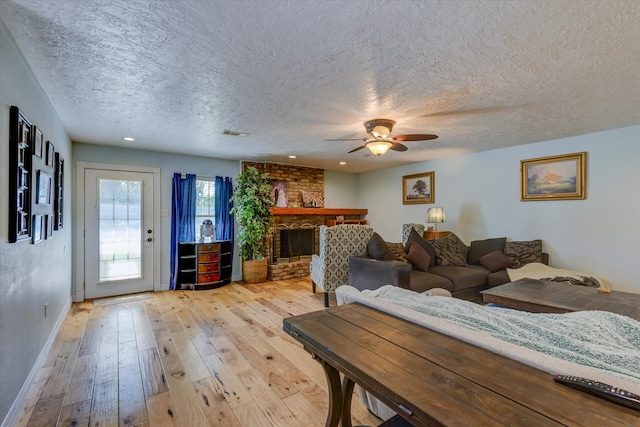 living room featuring light hardwood / wood-style floors, a textured ceiling, ceiling fan, and a brick fireplace