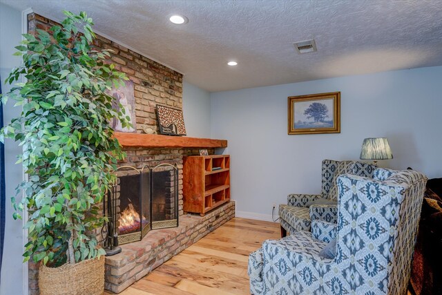 living area featuring hardwood / wood-style floors, a brick fireplace, and a textured ceiling