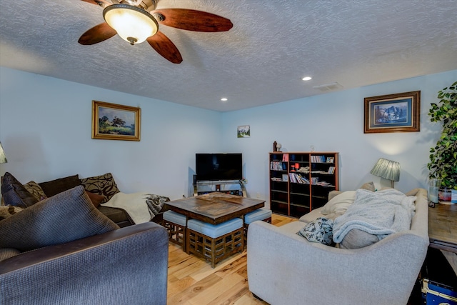 living room with light hardwood / wood-style flooring, a textured ceiling, and ceiling fan