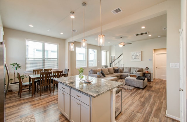 kitchen featuring hardwood / wood-style floors, light stone counters, ceiling fan, white cabinetry, and a center island