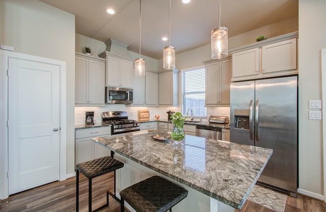 kitchen with a kitchen bar, a center island, stainless steel appliances, pendant lighting, and dark wood-type flooring