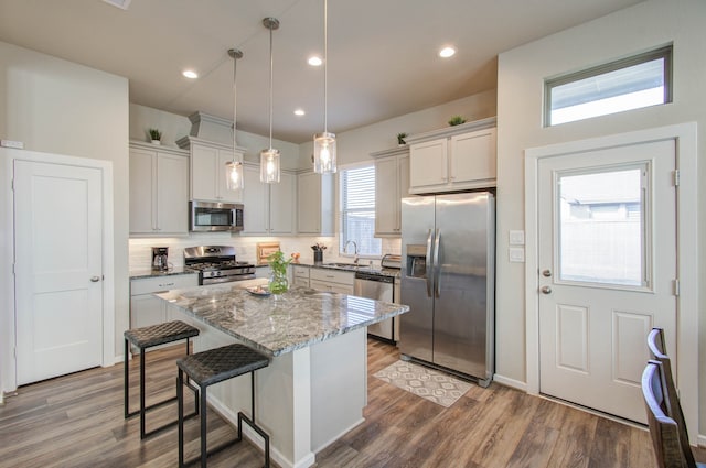 kitchen featuring wood-type flooring, appliances with stainless steel finishes, sink, a kitchen island, and pendant lighting