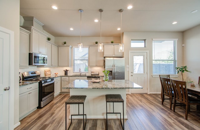 kitchen featuring hardwood / wood-style flooring, appliances with stainless steel finishes, a center island, and decorative light fixtures