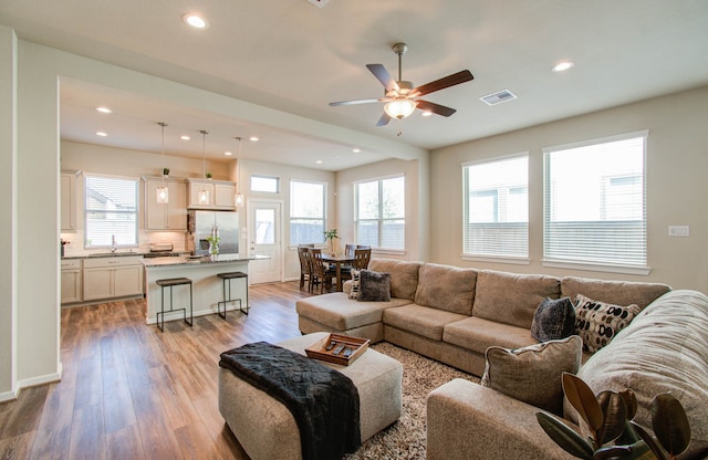 living room featuring ceiling fan, sink, and light wood-type flooring