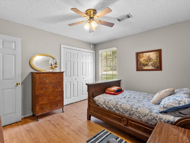 bedroom featuring light hardwood / wood-style flooring, a textured ceiling, a closet, and ceiling fan