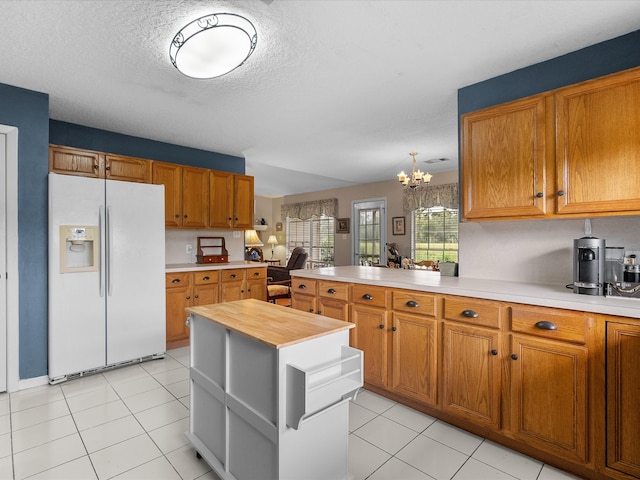 kitchen with a notable chandelier, white refrigerator with ice dispenser, light tile patterned floors, and kitchen peninsula