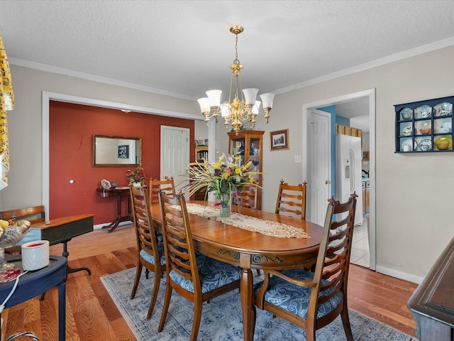 dining area with light hardwood / wood-style floors, a notable chandelier, a textured ceiling, and ornamental molding