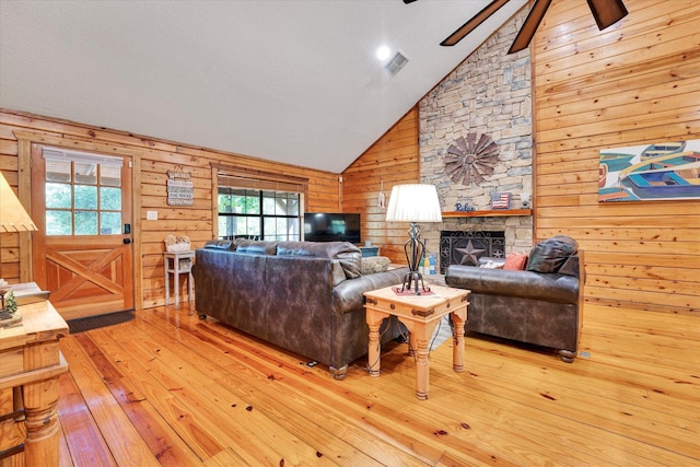 living room featuring vaulted ceiling, wood walls, light hardwood / wood-style flooring, and plenty of natural light